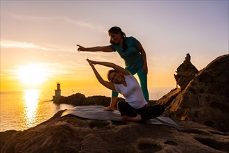 A yoga instructor working with the student in nature by the sea at sunset