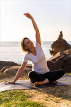 A blonde woman doing yoga exercises in nature by the sea