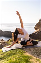 A latin woman doing yoga exercises in nature by the sea