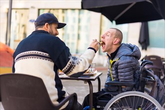 A disabled person eating with the help of a brother having fun