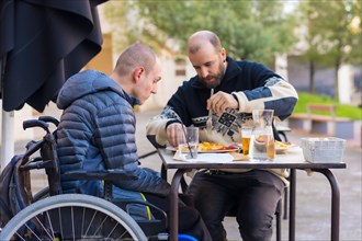 A disabled person eating on the terrace of a restaurant with a friend having fun