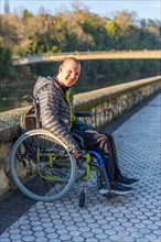 Portrait of a disabled person in a wheelchair smiling next to a river in a park