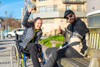 Portrait of disabled person in wheelchair with friend sitting having fun in the street