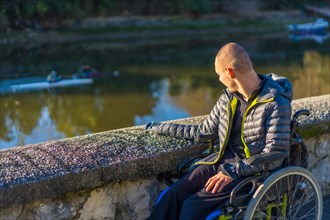 A disabled person in a wheelchair in a park looking at the river