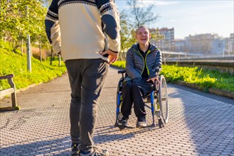 Disabled person in a wheelchair smiling with a family member taking a walk in a park