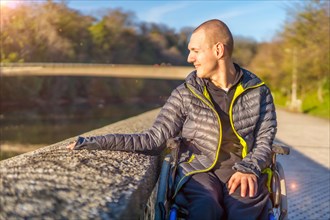 A disabled person in a wheelchair in a park at sunset next to a river at sunset