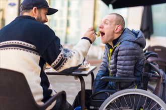 A disabled person eating with the help of a friend having fun