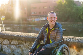 A disabled person in a wheelchair next to a river in the city sunset