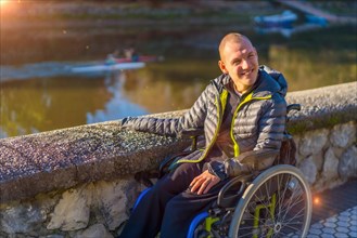 A disabled person in a wheelchair in a park at sunset smiling