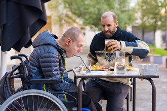 A disabled person eating on the terrace of a restaurant with a friend having fun