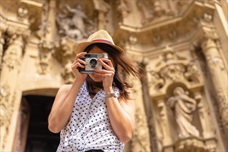 A woman in a hat visiting the city and taking photos with a vintage camera