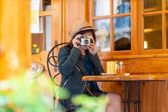 A tourist girl with a hat and a photo camera drinking tea on a cafe terrace
