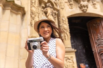 Smiling female tourist in hat visiting a church and taking photos with a camera