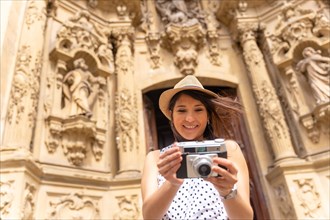 Tourist woman smiling with hat visiting the city and taking photos with a camera