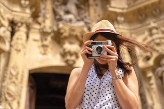 A woman in a hat visiting the city and taking photos with a vintage camera