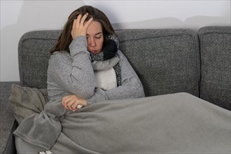 Sick woman with tissue paper with her cat covered with a blanket on her sofa