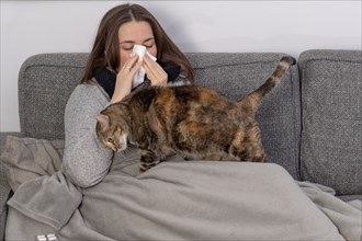 Sick woman with tissue paper with her cat covered with a blanket on her sofa