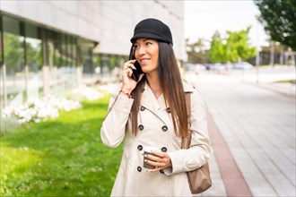 Businesswoman with a coffee in her hand and smiling talking on the phone outside the office