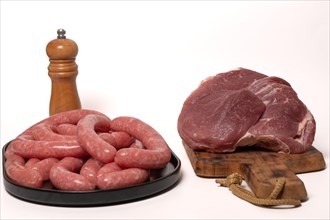 Fresh raw sausages on a black tray and Veal sirloin steak raw on a wooden board isolated on a white background