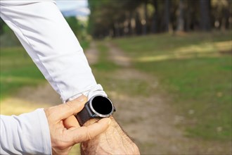 Man training in the field with his smart watch wearing black pants and white t-shirt a pine forest in the background