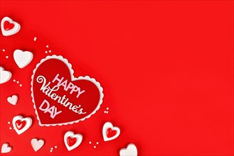 Valentine's Day flat lay with heart with text 'Happy Valentine's Day' and heart ornaments on red background with copy space