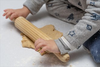 Boy kneading cookie dough with a wooden rolling pin and his brothers and mothers hands in the background