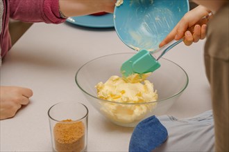 Children with their mother preparing a cake mixing the ingredients butter in the foreground