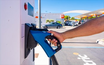 A man picking up the electric car charger at a gas station