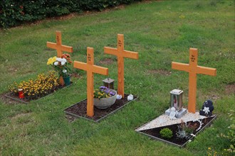 Flower decorated anonymous urn graves with wooden cross with inscription Here rests in God