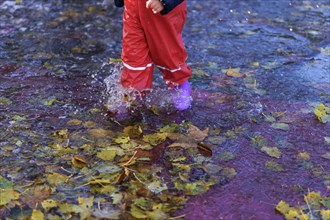 Child splashing water with boots and water pants in a puddle on a rainy day