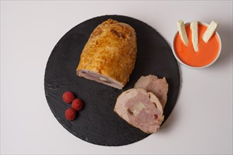 Close-up of a chicken stuffed with raspberry and goat cheese with a bowl of raspberry sauce isolated on white background