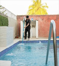 Maintenance person cleaning a swimming pool with skimmer
