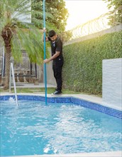 Young man cleaning a swimming pool with a vacuum hose