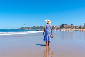 An elderly woman with a hat walking on the beach in Biarritz