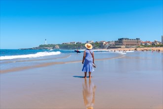 An elderly woman with a hat walking on the beach in Biarritz