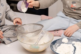 Children adding flour to a large sieve for a cake mixture