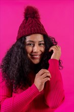 Curly-haired woman in a wool cap on a pink background portrait smiling