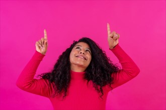 Curly-haired woman pointing up on a pink background