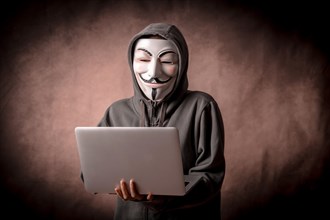 Man with anonymous mask with sweatshirt and with a laptop