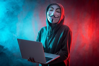 Hacker with anonymous mask with a computer and with a background of smoke and colored led