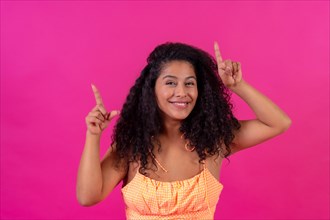 Curly-haired woman in summer clothes on a pink background pointing up
