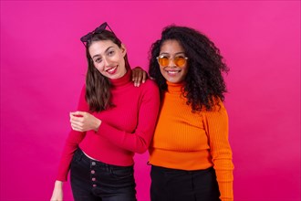 Portrait female friends in sunglasses having fun on a pink background