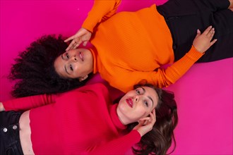 Two multi-ethnic women in a fashion posed on a pink background