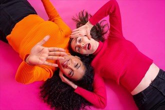 Two multi-ethnic women lying down making stop gesture with hands over pink background
