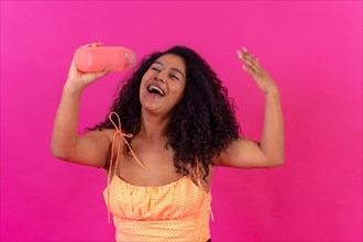 Curly-haired woman in summer clothes on a pink background drinking heated water