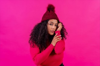 Curly-haired woman in a woolen cap on a pink background portrait with cold