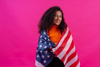 Curly-haired woman embracing usa flag on a pink background