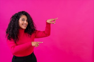 Curly-haired woman pointing to the right on a pink background