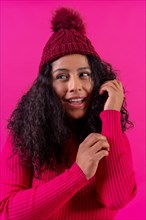 Curly-haired woman in a wool cap on a pink background portrait smiling
