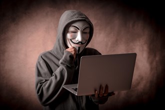 Hacker with anonymous mask with a laptop thinking about programming